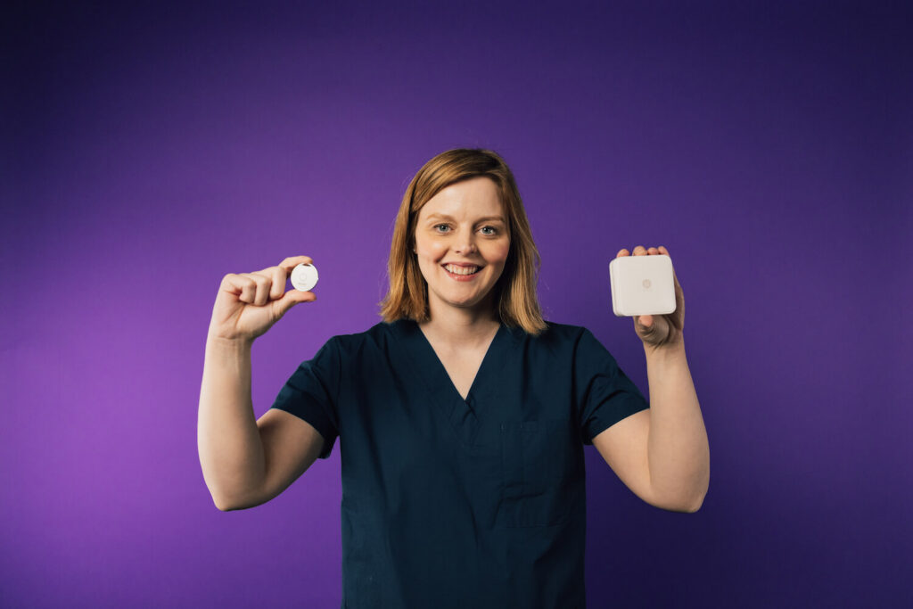 Smiling nurse in scrubs holding up a ROAR wearable panic button and a square beacon