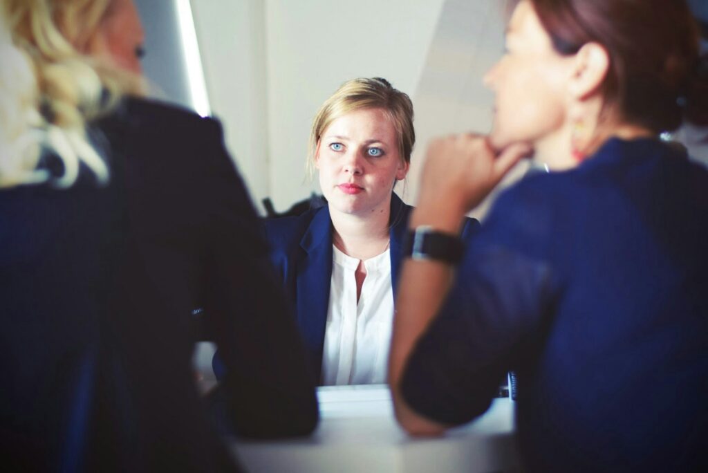 A teacher sits across a table facing two other people during a tense meeting.